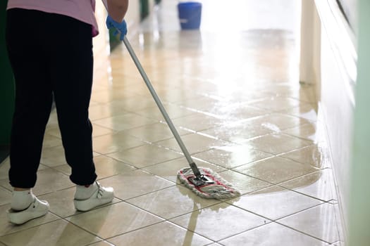 Female janitor standing in a hospital corridor with mop and bucket, symbolizing cleanliness and hygiene.