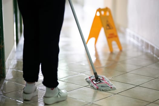 Female janitor standing in a hospital corridor with mop and bucket, symbolizing cleanliness and hygiene.
