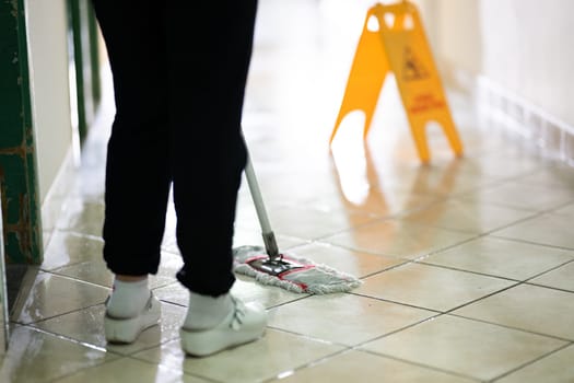 Female janitor standing in a hospital corridor with mop and bucket, symbolizing cleanliness and hygiene.