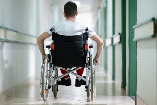 Young teenage boy smiling while sitting in a wheelchair in a hospital hallway. Rehabilitation and positivity concept