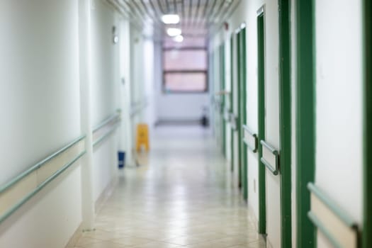 Bright and clean hospital corridor with green doors and handrails, illuminated by natural daylight through windows.