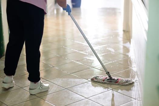 Female janitor standing in a hospital corridor with mop and bucket, symbolizing cleanliness and hygiene.