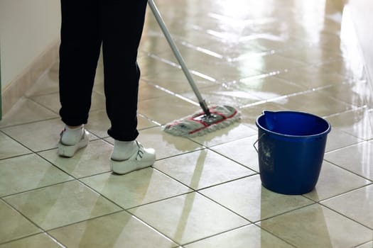 Female janitor standing in a hospital corridor with mop and bucket, symbolizing cleanliness and hygiene.
