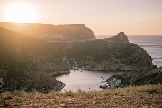 A beautiful sunset over a mountain with a small town in the distance. The sun is setting behind the mountains, casting a warm glow over the landscape. The water in the valley is calm and peaceful