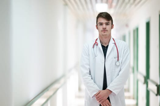 Young male doctor standing confidently in a hospital corridor with a stethoscope. Medical professionalism concept.