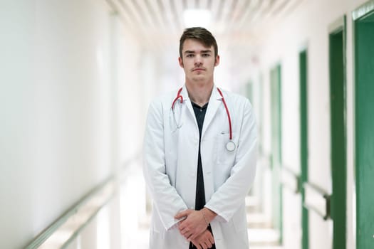 Young male doctor standing confidently in a hospital corridor with a stethoscope. Medical professionalism concept.