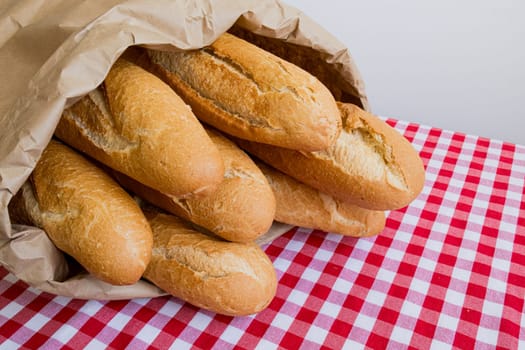 Fresh baguettes in paper bag on red and white checkered tablecloth.
