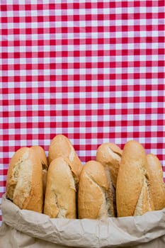 Fresh baguettes in paper bag on red gingham tablecloth background.