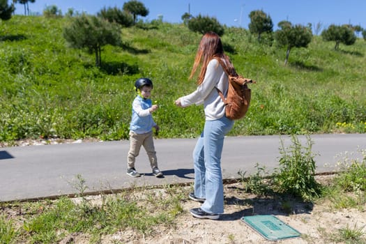Child wearing helmet giving flower to mother in park during sunny day