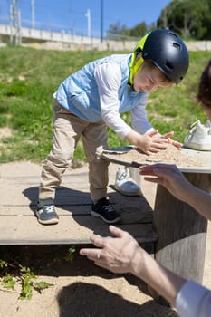 Young boy wearing a helmet playing with sand on a playground table, supervised by a therapist