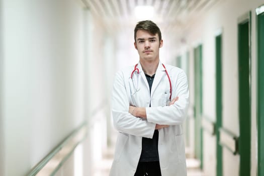 Young male doctor standing confidently in a hospital corridor with a stethoscope. Medical professionalism concept.