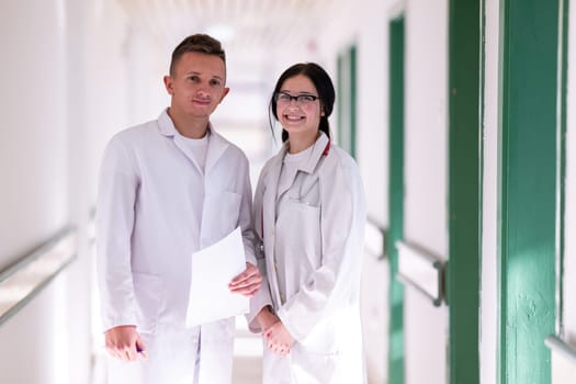 Two doctors in white coats walking and discussing medical documents in a brightly lit hospital corridor, emphasizing teamwork and professional healthcare environment.