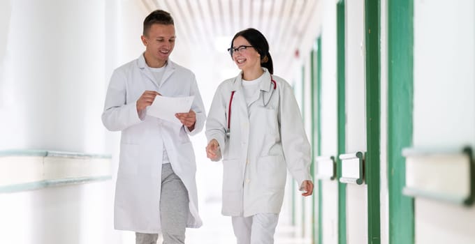 Two doctors in white coats walking and discussing medical documents in a brightly lit hospital corridor, emphasizing teamwork and professional healthcare environment.