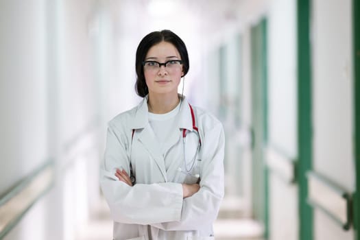 Confident young female doctor with a stethoscope smiling while standing in a bright hospital corridor.