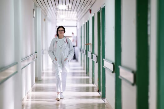 Confident young female doctor with a stethoscope smiling while standing in a bright hospital corridor.