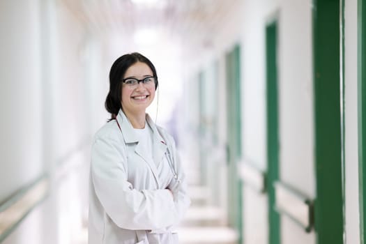 Confident young female doctor with a stethoscope smiling while standing in a bright hospital corridor.