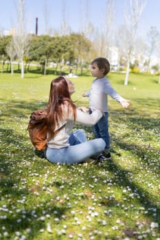 Mother sitting on the grass interacting with her son in a park full of daisies