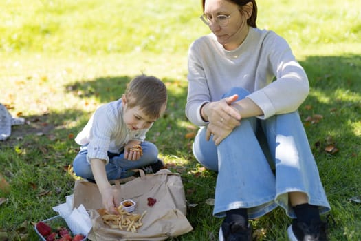 Mother and son having a picnic lunch of fast food in a park, enjoying quality time together outdoors