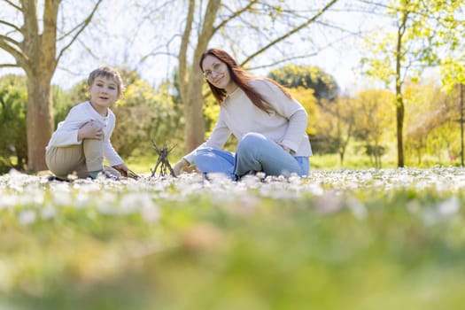 Mother and son building a small stick house together in a field of white flowers in springtime