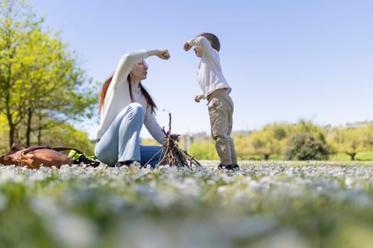 Mother and son having fun building a small bonfire together in a field of flowers on a sunny day