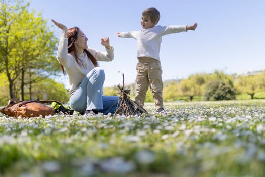 Mother and son are playing in a field of flowers and building a small bonfire on a sunny day