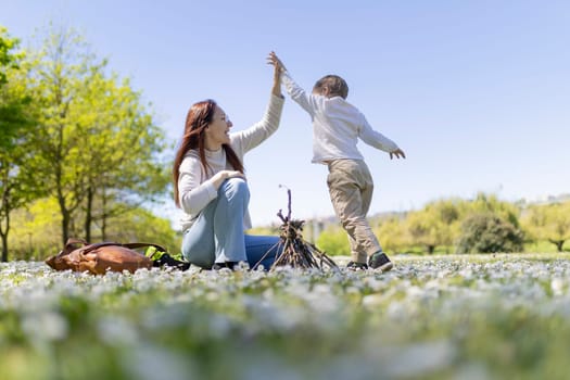 Mother and son having fun in a field of flowers, building a small bonfire on a bright sunny day