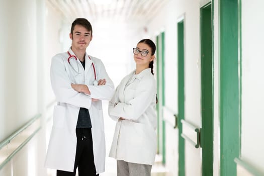 Male and female doctors in white coats posing confidently in hospital hallway. Teamwork and healthcare concept.