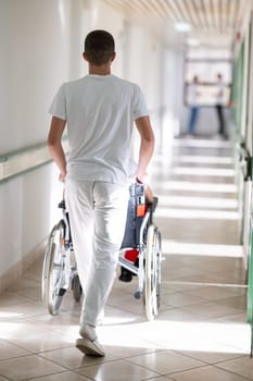 Medical staff in white uniforms assist a patient in a wheelchair in a bright hospital corridor. Concept of healthcare and assistance.