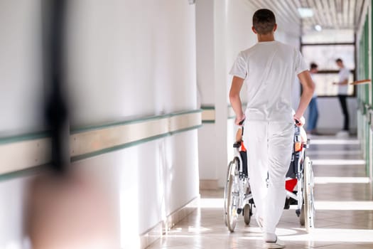 Medical staff in white uniforms assist a patient in a wheelchair in a bright hospital corridor. Concept of healthcare and assistance.
