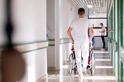 Medical staff in white uniforms assist a patient in a wheelchair in a bright hospital corridor. Concept of healthcare and assistance.