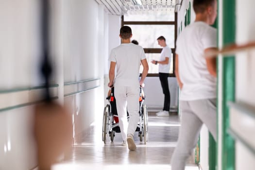 Medical staff in white uniforms assist a patient in a wheelchair in a bright hospital corridor. Concept of healthcare and assistance.