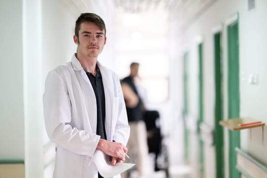 Young male doctor walking in hospital hallway while reading patient documentation. Clinical work environment.