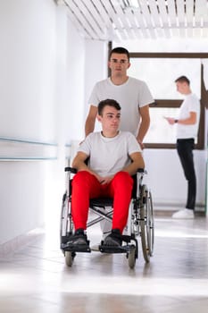 A smiling young man in a wheelchair is being pushed by a female healthcare worker in a white coat and stethoscope. They are in a hospital corridor, suggesting a medical or rehabilitation environment, evoking care and recovery.