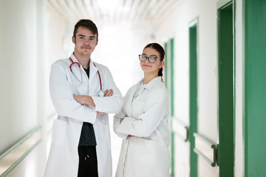 Male and female doctors in white coats posing confidently in hospital hallway. Teamwork and healthcare concept.