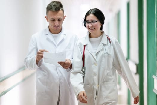 Two doctors in white coats walking and discussing medical documents in a brightly lit hospital corridor, emphasizing teamwork and professional healthcare environment.
