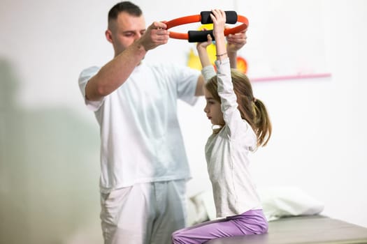 Young girl performing rehabilitation exercises with the help of a trainer, using a resistance ring while lying on a medical bench.