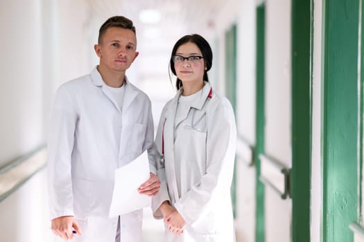 Two doctors in white coats walking and discussing medical documents in a brightly lit hospital corridor, emphasizing teamwork and professional healthcare environment.