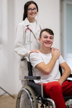 A smiling young man in a wheelchair is being pushed by a female healthcare worker in a white coat and stethoscope. They are in a hospital corridor, suggesting a medical or rehabilitation environment, evoking care and recovery.