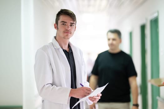 Young male doctor walking in hospital hallway while reading patient documentation. Clinical work environment.