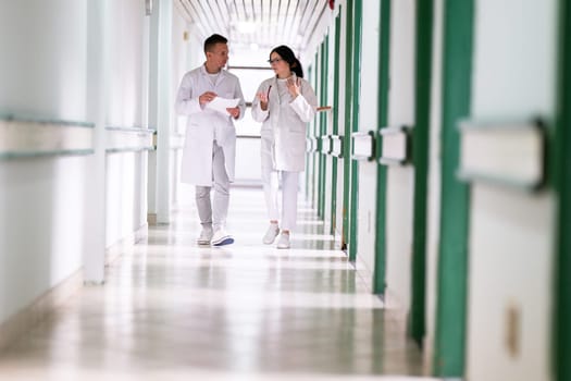 Two doctors in white coats walking and discussing medical documents in a brightly lit hospital corridor, emphasizing teamwork and professional healthcare environment.