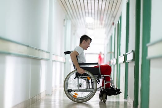 Young teenage boy smiling while sitting in a wheelchair in a hospital hallway. Rehabilitation and positivity concept