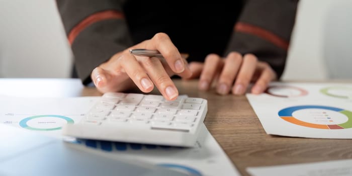 A business professional using a calculator while analyzing financial data and charts, emphasizing precision and analytical skills.