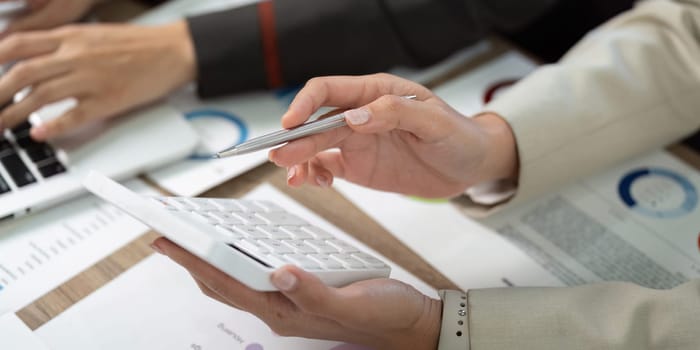 Two professionals collaborate on financial reports, using a calculator and charts to guide their discussion.