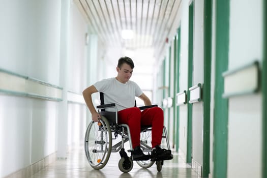 Young teenage boy smiling while sitting in a wheelchair in a hospital hallway. Rehabilitation and positivity concept