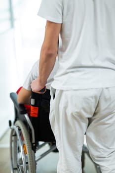 Medical staff in white uniforms assist a patient in a wheelchair in a bright hospital corridor. Concept of healthcare and assistance.