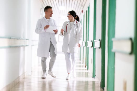 Two doctors in white coats walking and discussing medical documents in a brightly lit hospital corridor, emphasizing teamwork and professional healthcare environment.