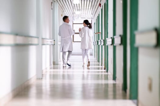 Two doctors in white coats walking and discussing medical documents in a brightly lit hospital corridor, emphasizing teamwork and professional healthcare environment.