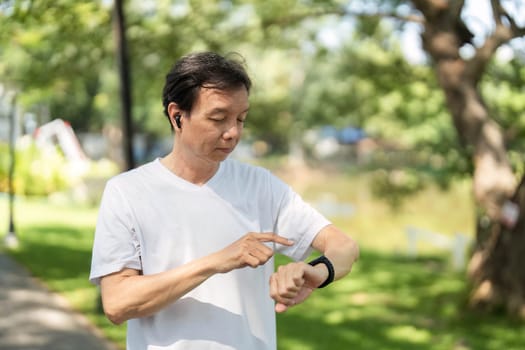 An elderly man checks his smartwatch while exercising in a park, promoting wellness and active living in later years.