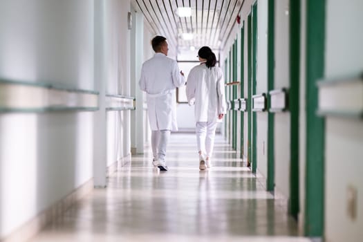 Two doctors in white coats walking and discussing medical documents in a brightly lit hospital corridor, emphasizing teamwork and professional healthcare environment.
