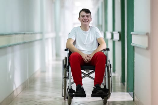 Young teenage boy smiling while sitting in a wheelchair in a hospital hallway. Rehabilitation and positivity concept